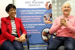 Valerie and Austin sit smiling in front of an informational banner at a Foster for East Midlands event