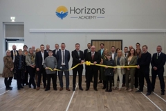 Councillors, representatives from the Trust are lined up in the school hall holding a yellow ribbon to help celebrate that the academy is now open 
